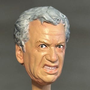 May include: A highly detailed, hand-painted miniature head sculpt of an older individual with grey hair. The figure features a distinct facial expression with a furrowed brow, wide eyes, and a bared-teeth grimace, showcasing realistic skin tones.