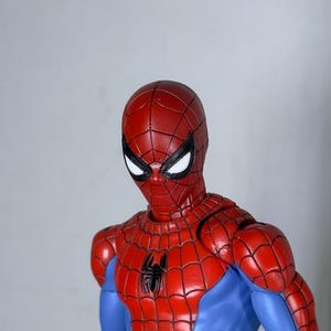 Puede incluir: Figura de acci&oacute;n de Spider-Man rojo y azul. La figura tiene una m&aacute;scara roja con ojos blancos y un emblema de ara&ntilde;a negra en el pecho. La figura lleva un traje rojo y azul con un patr&oacute;n de telara&ntilde;a.