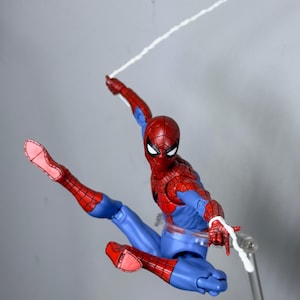 Puede incluir: Figura de acci&oacute;n de Spider-Man, rojo y azul, en una pose din&aacute;mica, con una telara&ntilde;a blanca que se extiende desde la mano de la figura. La figura est&aacute; en el aire, con una pierna extendida. La figura est&aacute; sobre un soporte transparente.