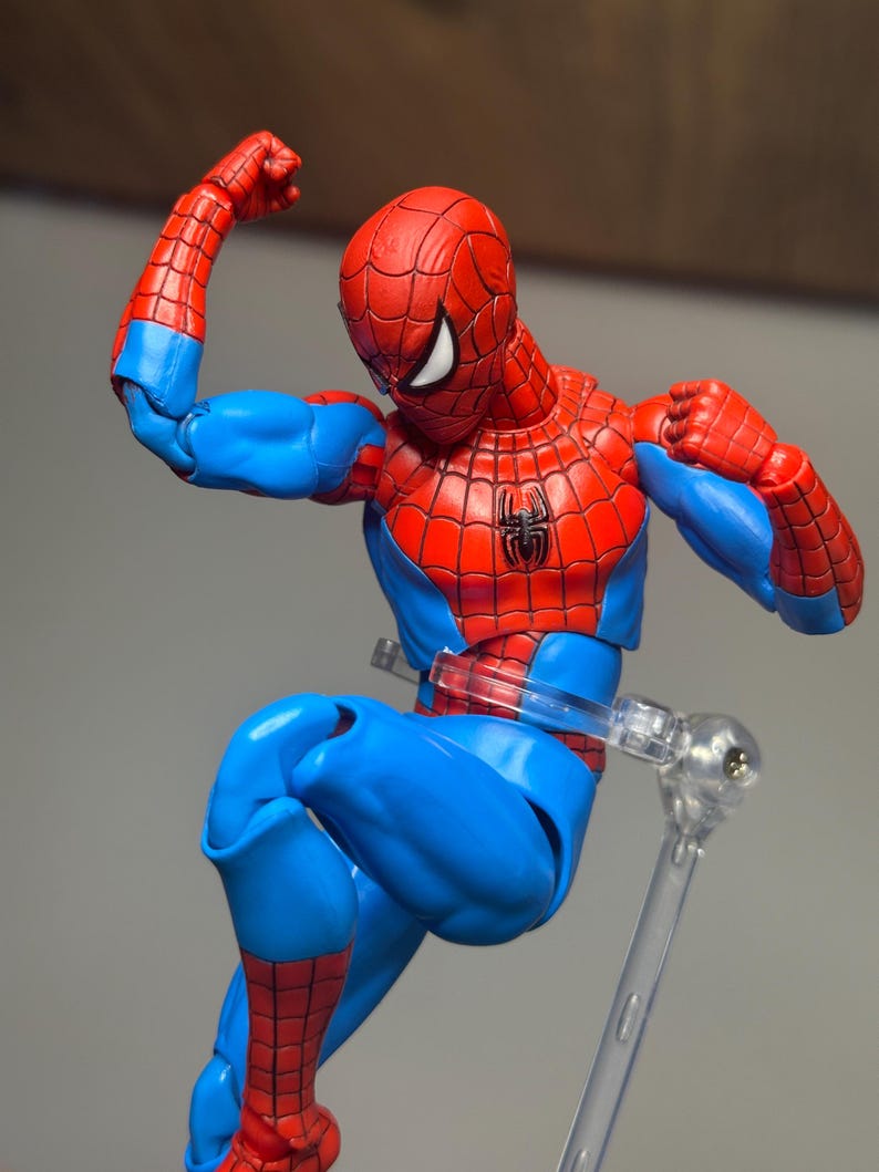 May include: A Spider-Man action figure in a dynamic pose, featuring a red and blue costume with a spider emblem on the chest. The figure is supported by a clear stand, showcasing the character's iconic design and colors.