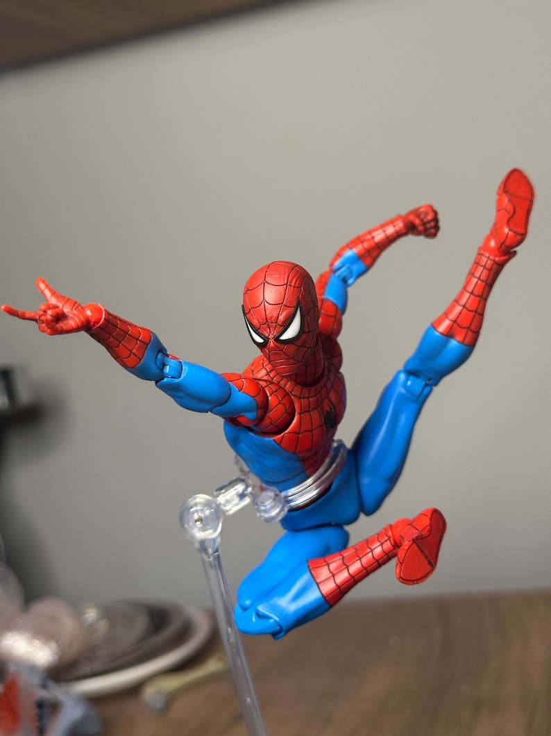 May include: A Spider-Man action figure in a dynamic pose, featuring a red and blue costume. The figure has a detailed web pattern on the red sections, with a white-eyed mask. The figure is supported by a clear stand, showcasing its acrobatic stance.