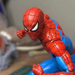May include: A red and blue Spider-Man action figure in a dynamic pose. The figure features a detailed red mask with white eye lenses, a red and blue suit, and articulated joints. The figure is posed as if ready for action.