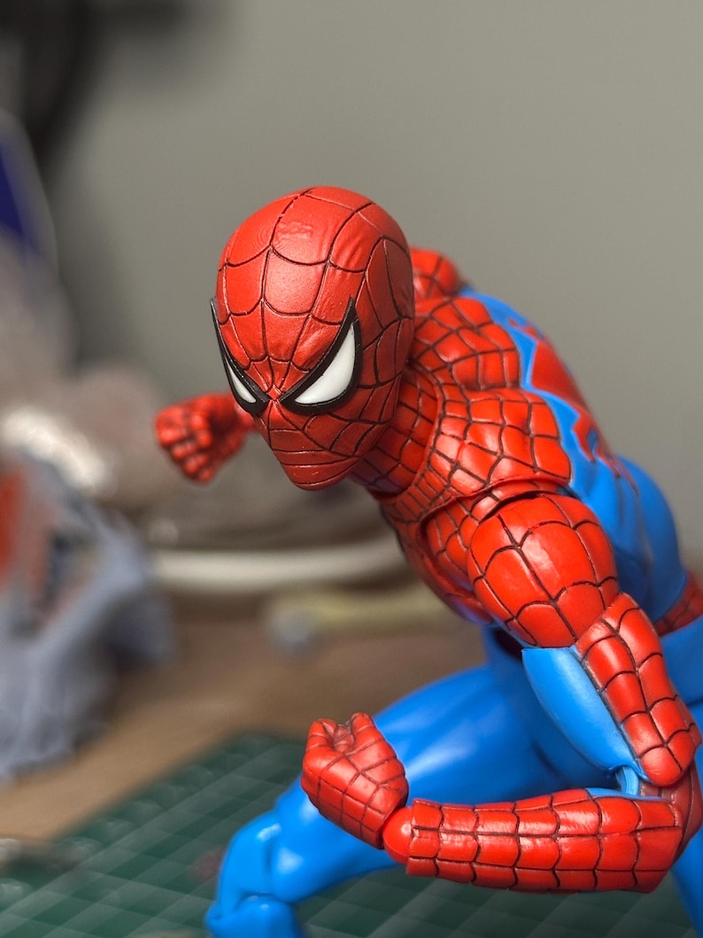May include: A red and blue Spider-Man action figure in a dynamic pose. The figure features a detailed red mask with white eye lenses, a red and blue suit, and articulated joints. The figure is posed as if ready for action.