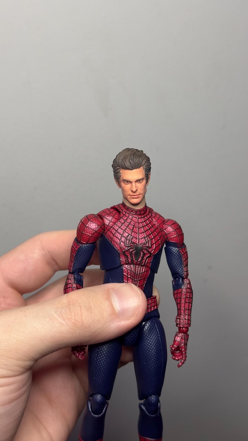 Może przedstawiać: Figurka Spider-Mana w klasycznym czerwono-niebieskim kostiumie. Figurka ma szczeg&oacute;łowy wz&oacute;r pajęczyny na czerwonych częściach i czarny emblemat pająka na klatce piersiowej. Figurka jest trzymana w dłoni.