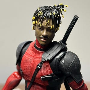 Puede incluir: Figura de acción detallada de un personaje con rastas negras y amarillas, un bigote y un traje rojo y negro. La figura tiene una espada en la espalda y una hebilla de cinturón con un diseño circular.