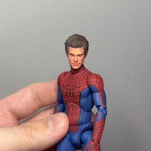 Może przedstawiać: Szczeg&oacute;łowa figurka Spider-Mana w klasycznym kostiumie. Figurka ma czerwono-niebieski kostium z detalami pajęczyny, czerwony emblemat pająka na klatce piersiowej i realistyczną rzeźbę głowy. Figurka ma około 15 cm wysokości.