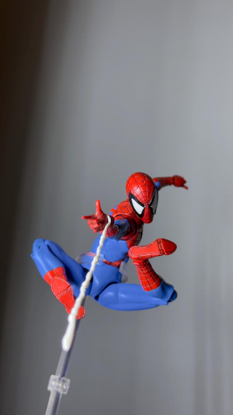 Puede incluir: Figura de acci&oacute;n de Spider-Man en pose din&aacute;mica, con un traje rojo y azul con detalles de telara&ntilde;a. La figura est&aacute; en el aire, con una telara&ntilde;a blanca que se extiende desde su mano. La m&aacute;scara tiene lentes blancas.