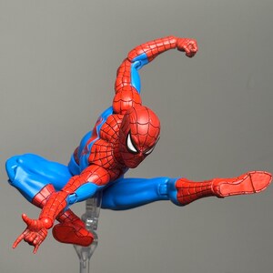May include: A Spider-Man action figure in a dynamic pose, featuring a red and blue costume. The figure is mid-air, with one arm extended and the other bent, showcasing the character's iconic web-slinging stance. The figure is on a clear stand.