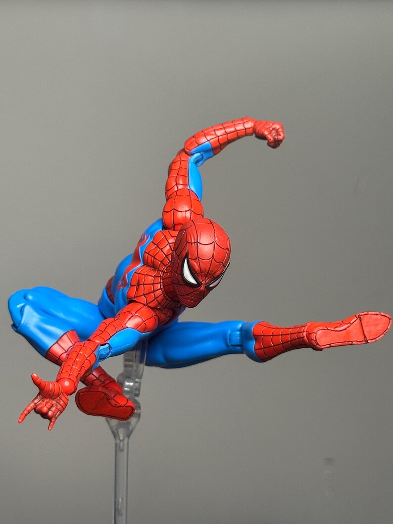 May include: A Spider-Man action figure in a dynamic pose, featuring a red and blue costume. The figure is mid-air, with one arm extended and the other bent, showcasing the character's iconic web-slinging stance. The figure is on a clear stand.