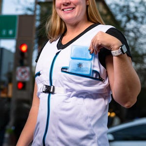 Può includere: Gilet rinfrescante bianco con finiture nere e cerniera turchese. Il gilet ha due tasche contenenti ghiaccioli blu. Il gilet è progettato per mantenere fresco chi lo indossa.