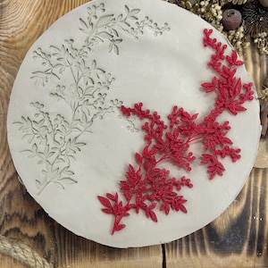 May include: A round, off-white decorative piece with floral designs. One side features an embossed floral pattern, while the other side has a vibrant red, three-dimensional floral embellishment. The piece is set against a rustic wooden background.