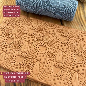 Puede incluir: Un rodillo de arcilla marrón y un rodillo gris con un patrón repetido de setas, corazones y hojas. La arcilla marrón tiene el mismo patrón en relieve. El texto de la imagen dice "SUITABLE FOR POTTERY CLAY POLYMER CLAY AIR DRY CLAY".