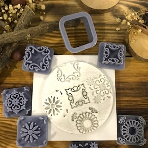May include: A selection of grey stamps featuring floral and geometric patterns. The stamps are square and rectangular, with a square frame and a circular stamp also visible. The items are arranged on a wooden surface.