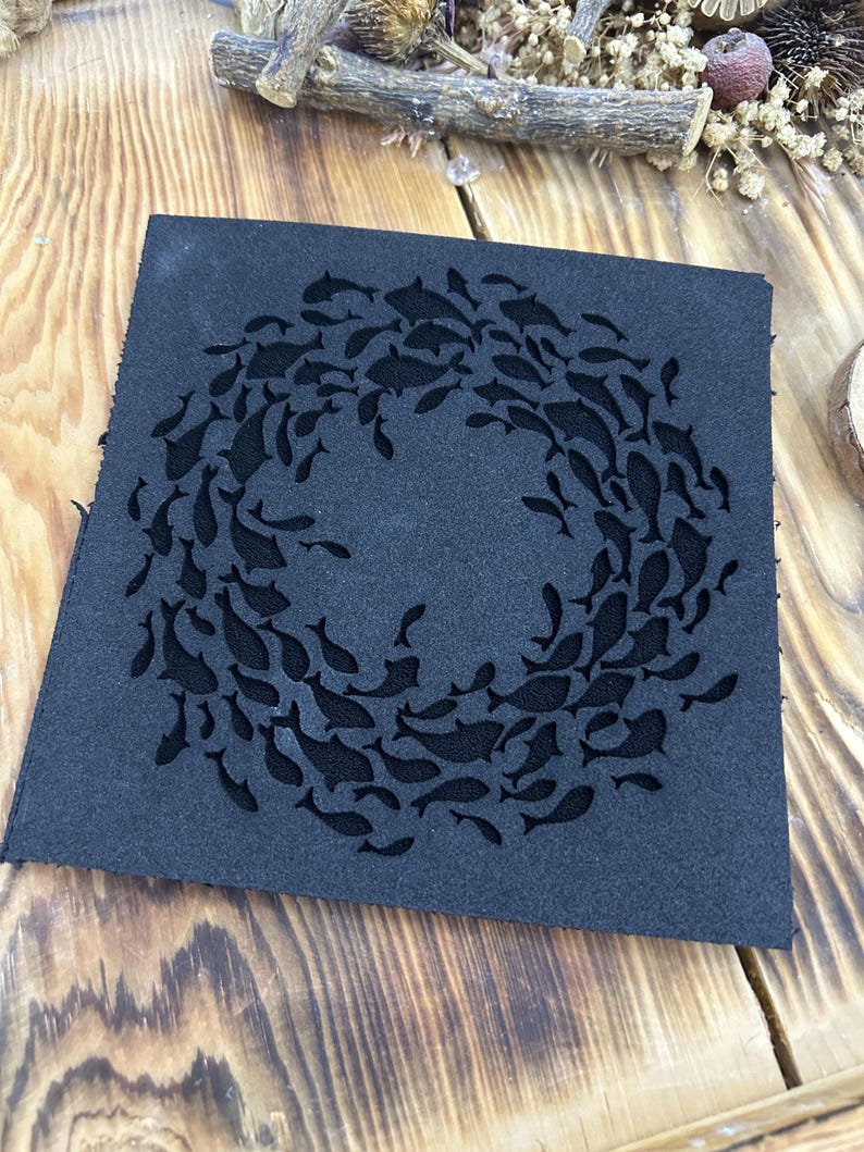 May include: A square, dark blue piece of fabric with a circular design of cutout fish. The fish are arranged in a ring, creating a decorative pattern. The fabric has a slightly textured surface.