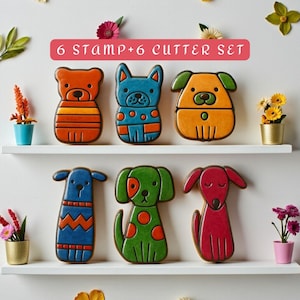 May include: A collection of six dog-shaped cookie cutters and stamps in shades of orange, blue, green, and red. The set is labelled "6 STAMP+6 CUTTER SET" in a pink rectangle. The cutters are presented on a white shelf, decorated with flowers.