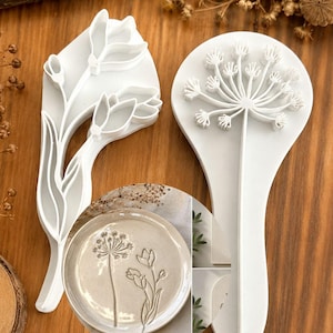 Peut inclure: Deux emporte-pièces en plastique blanc pour argile avec des motifs botaniques. L'un représente une tige de tulipe avec des feuilles, l'autre est un outil circulaire avec un motif de pissenlit ou d'ail. Un petit encart montre l'argile imprimée.