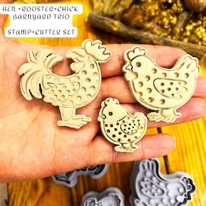 May include: A trio of beige cookie cutters depicting a rooster, hen, and chick. The rooster has a detailed tail and comb. The hen and chick have rounded forms. The text "HEN + ROOSTER + CHICK BARNYARD TRIO STAMP + CUTTER SET" is visible.