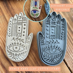 Può includere: Taglierina e timbro per argilla a forma di mano di Hamsa. L'immagine mostra una taglierina e un timbro per argilla dettagliati a forma di mano, con un disegno a occhio nel palmo. Il testo "DIFFERENT SIZES AVAILABLE" e "HAMSA HAND CLAY CUTTER+STAMP" sono visibili.