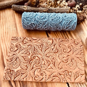 May include: A blue patterned roller and a brown rectangular piece with an octopus design. The roller is cylindrical and features a repeating octopus tentacle pattern. The rectangular piece has a similar embossed design. The items are on a wooden surface.