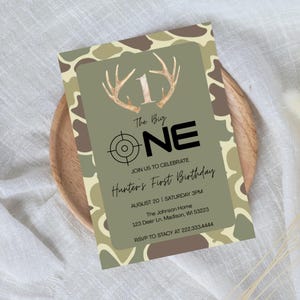 May include: A birthday invitation with a camouflage pattern border. The invitation features the text "The Big ONE" with a target graphic and antler accents. It reads "Hunter's First Birthday" with event details.