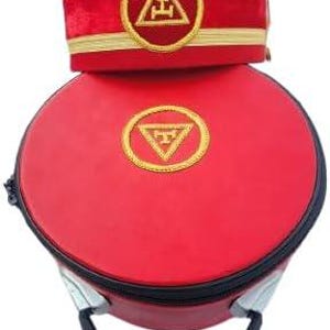 May include: A red ceremonial hat with gold trim and a matching red case. The hat features a gold emblem within a circle, and the case has a similar emblem. The case has a black handle and zipper.
