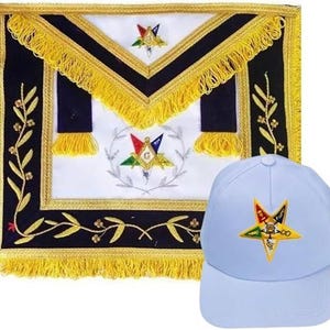 Puede incluir: Un delantal masónico con centro blanco, bordes negros y flecos dorados. El delantal presenta símbolos bordados y una gorra de béisbol azul claro con un emblema de estrella.