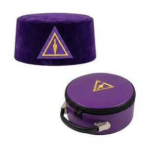 May include: A purple velvet fez hat with a gold and yellow emblem, and a matching round purple case with a handle. The case has a gold emblem on the top. The hat and case are on a white background.