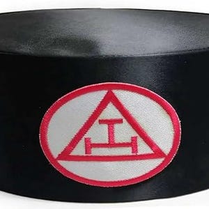 May include: Black cylindrical hat with a red and white emblem. The emblem features a red triangle and a horizontal bar design within a white circle. The hat is made of a smooth, dark material.