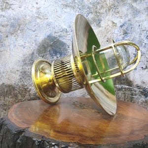 May include: A brass nautical wall sconce with a clear glass globe in a protective cage. The sconce has a circular base and a flared reflector, with a vintage aesthetic. The fixture is designed for wall mounting and has a polished finish, suitable for interior lighting.