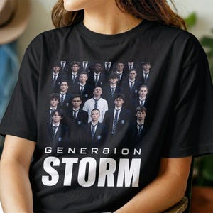 May include: A black short-sleeved t-shirt featuring a graphic print of a large group of individuals in formal suits and ties. Below the image, the text reads GENER8ION STORM in bold white capital letters, with the number 8 replacing the letter O.