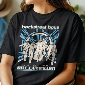 Puede incluir: Una camiseta negra de manga corta con un estampado gráfico de los Backstreet Boys. El diseño incluye el texto "backstreet boys" e "INTO THE MILLENNIUM" en blanco y azul, con una ilustración estilizada de los cinco miembros del grupo.