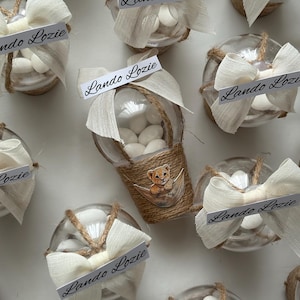 Può includere: Contenitori trasparenti in vetro per bomboniere riempiti di caramelle bianche, decorati con spago, fiocchi color crema ed etichette con la scritta "Lando Lozie". Un contenitore presenta una piccola illustrazione di cucciolo di leone. Ideale per eventi.