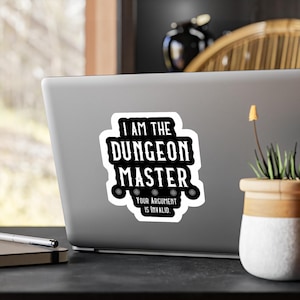 Puede incluir: Una pegatina blanca con el texto "I AM THE DUNGEON MASTER Your Argument Is Invalid" en negrita, en negro. La pegatina tiene un borde negro y está pegada a un portátil. La pegatina es un artículo divertido para los fanáticos de los juegos de rol de mesa.