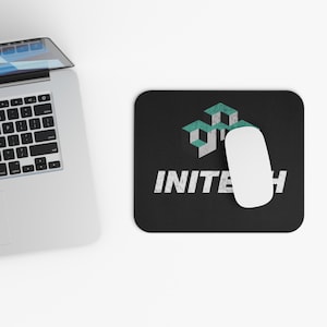 Puede incluir: Alfombrilla de ratón rectangular negra con la palabra "INITECH" en blanco, un ratón blanco y un diseño geométrico turquesa y blanco. Un ordenador portátil es parcialmente visible en la esquina superior izquierda.