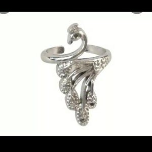 Puede incluir: Un anillo plateado con forma de pavo real. El anillo presenta un diseño curvo con una cabeza de pavo real y una cola en abanico. El anillo está hecho de metal brillante y está sobre un fondo blanco.