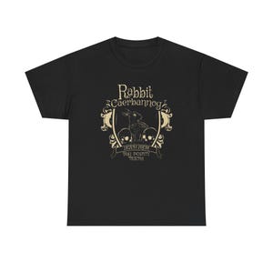 Könnte beinhalten: Schwarzes T-Shirt mit einem Grafikdesign. Das Design enthält den Text "Rabbit Caerbannog" über einer Illustration eines Kaninchens und zwei Totenköpfen. Der Text "Death from Big Pointy Teeth" befindet sich darunter.
