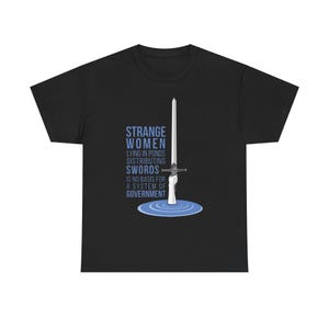 May include: Black t-shirt featuring the text "STRANGE WOMEN LYING IN PONDS DISTRIBUTING SWORDS IS NO BASIS FOR A SYSTEM OF GOVERNMENT" and a sword graphic. The design is in blue and white.