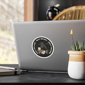 May include: A round sticker featuring a black crow with a coffee cup, perched on books. The sticker has the text "Highly Intelligent - Mildly Unstable - Barely Functional" in a circular design with stars.