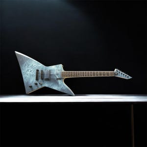 Könnte beinhalten: Eine E-Gitarre mit scharfem, kantigem Korpus in verwitterter grauer Optik. Auf dem Korpus steht der Text PLAGUE XXI CENTURY. Sie verfügt über zwei schwarze Humbucker-Tonabnehmer, eine feste Brücke, schwarze Regler und ein dunkles Griffbrett mit sechs Saiten.