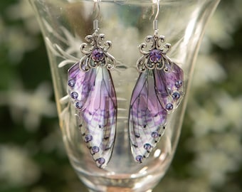 May include: A pair of silver earrings with purple and white butterfly wings and a clear crystal accent.