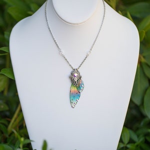 May include: A silver chain necklace with a iridescent butterfly wing pendant. The pendant is detailed with silver accents and a clear crystal in the center.