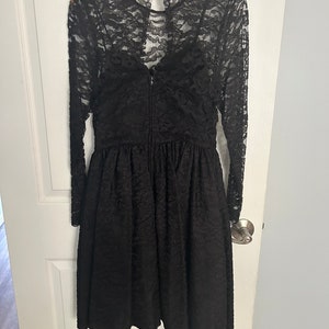 Pode incluir: Um vestido preto de renda com mangas compridas e decote redondo. O vestido tem um corpete justo e uma saia rodada.