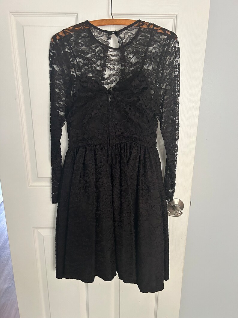 Pode incluir: Um vestido preto de renda com mangas compridas e decote redondo. O vestido tem um corpete justo e uma saia rodada.