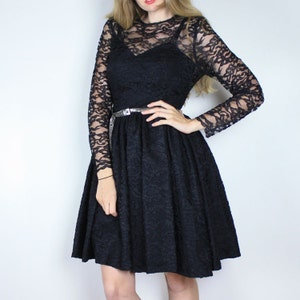 Pode incluir: Um vestido preto de renda com mangas compridas e um corpete justo. O vestido tem uma saia rodada e um cinto prateado.