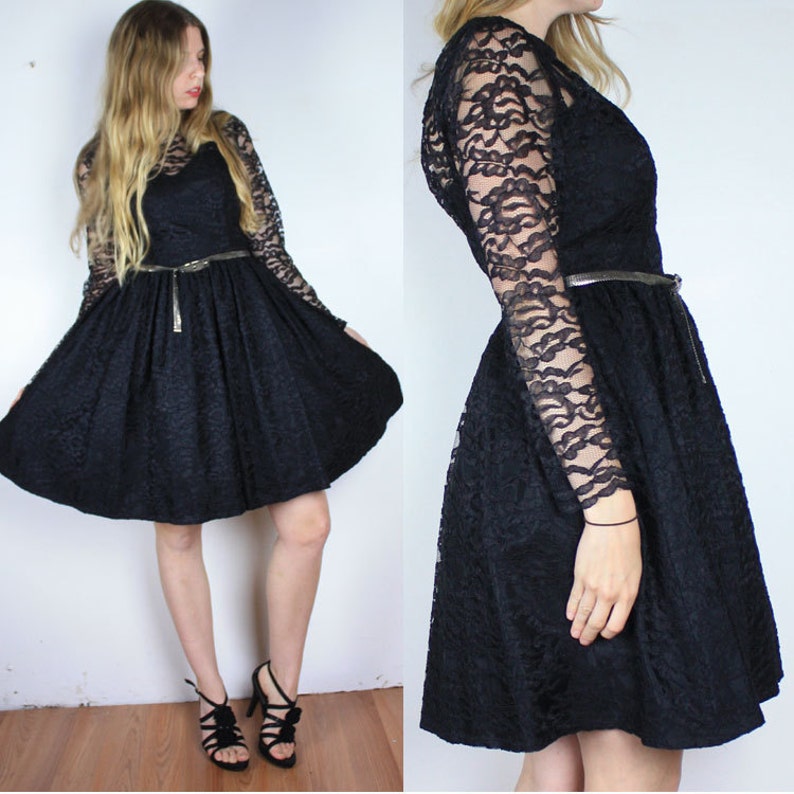 Pode incluir: Um vestido preto de renda com mangas compridas e saia rodada. O vestido tem um corpete justo e um cinto prateado.
