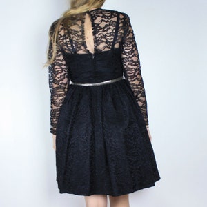 Pode incluir: Um vestido preto de renda com mangas compridas e um corpete justo. O vestido tem uma saia rodada e um cinto prateado.