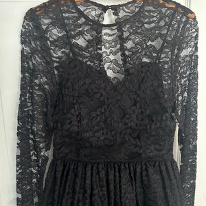 Pode incluir: Um vestido preto de renda com mangas compridas e decote redondo. O vestido tem um corpete justo e uma saia fluida.
