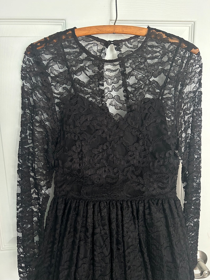 Pode incluir: Um vestido preto de renda com mangas compridas e decote redondo. O vestido tem um corpete justo e uma saia fluida.