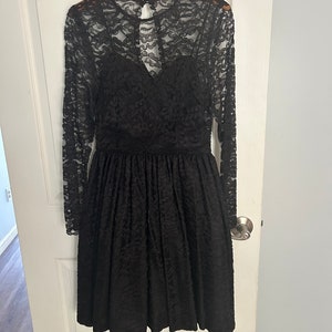 Pode incluir: Um vestido preto de renda com mangas compridas e um corpete justo. O vestido tem uma saia cheia e um decote nas costas em forma de fechadura.