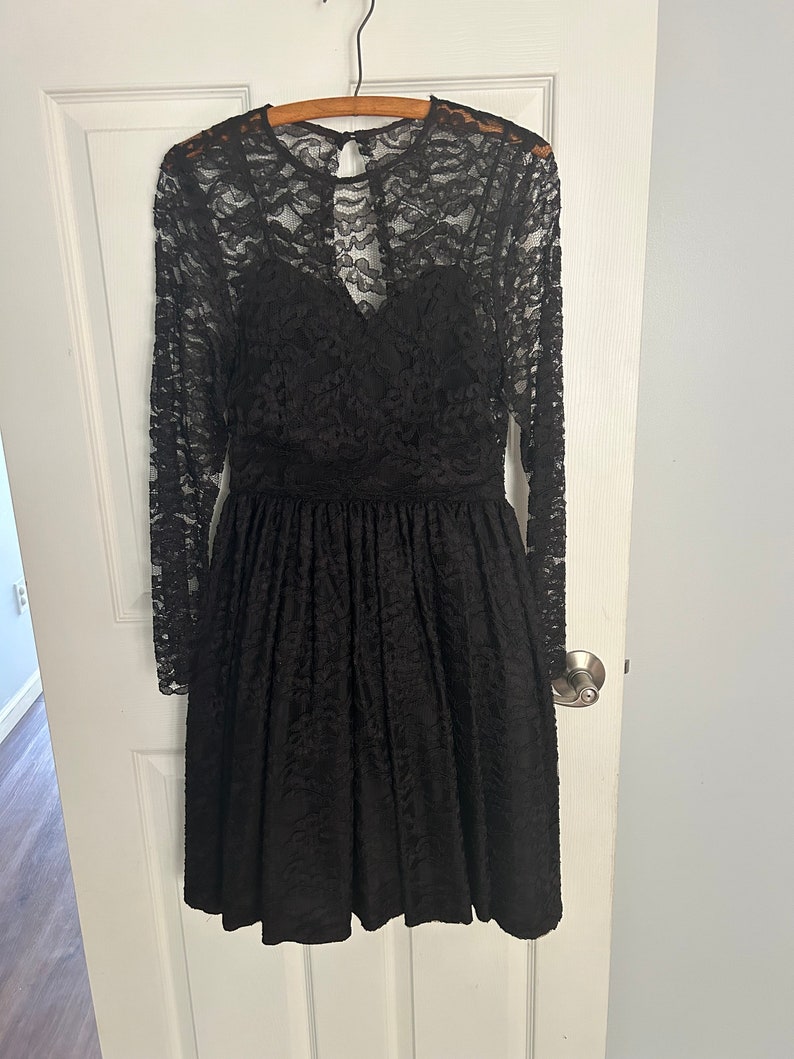 Pode incluir: Um vestido preto de renda com mangas compridas e um corpete justo. O vestido tem uma saia cheia e um decote nas costas em forma de fechadura.